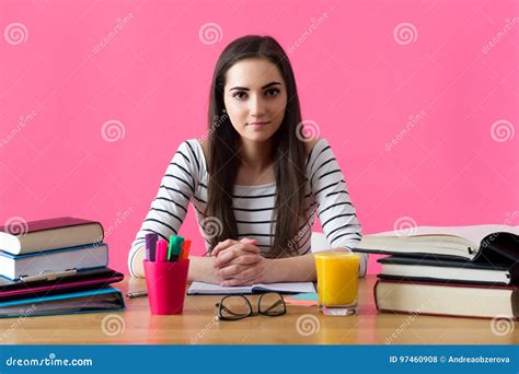 Smiling Female Student Sitting At Her Desk Filled With Textbooks Stock