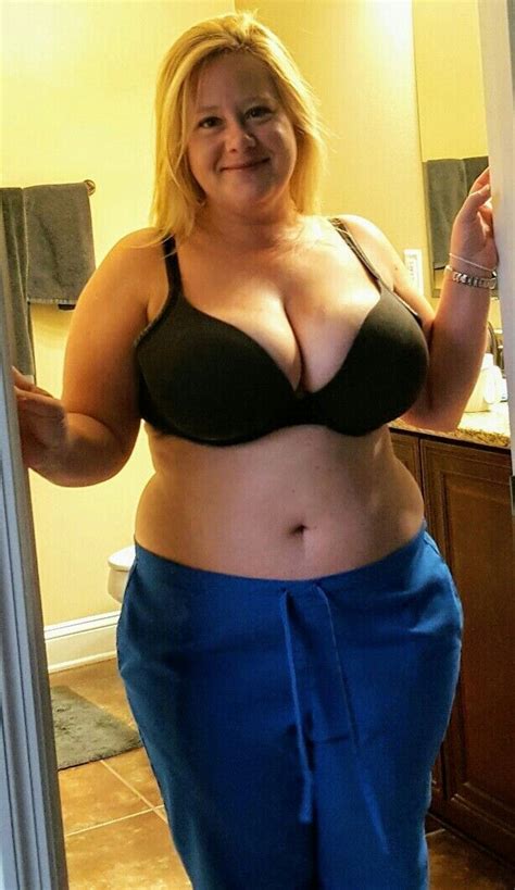A Woman In A Black Bra Top And Blue Pants Is Standing In Front Of A Mirror
