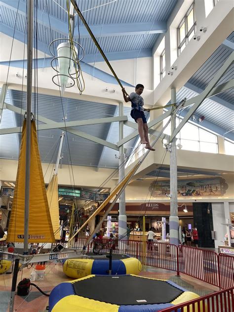 A Boy Is On The Ropes In An Indoor Area With Other Toys And People Around