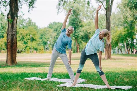 Mature Man And Woman Standing In Warrior Poses While Practicing Yoga In Park Stock Image Image
