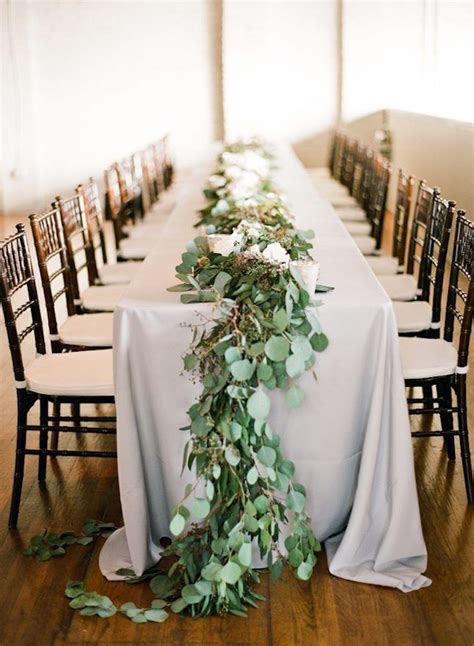 A Long Table With White Flowers And Greenery Is Set Up For A Wedding
