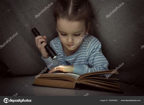 Little Girl Reading Fairy Tales Book Under The Covers At The Eve Stock