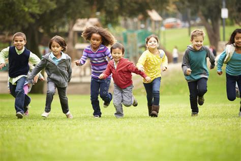 Group Of Young Children Running Towards Camera In Park Puddle Jumpers