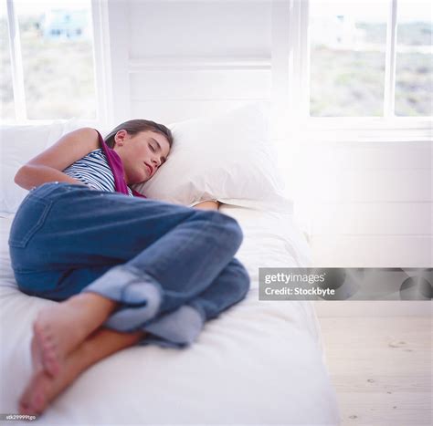 A Young Teenage Girl Sleeping On A Bed With Her Hand Under A Pillow