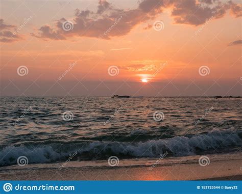 Waves Crash On Sandy Beach At Sunset With Vivid Orange Sky Stock Photo