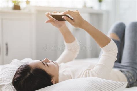 Young Woman Watching The Mobile Phone And Lying On The Bed At Home