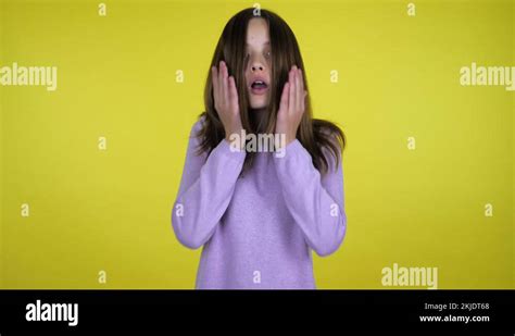 Teen Girl Raises Head And Shocked Puts Palms To Cheeks On A Yellow Background Stock Video