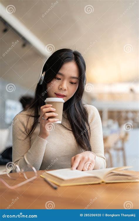 An Attractive Asian Woman Is Sipping Coffee And Listening To Music While Reading A Book Stock