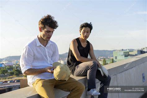 Two Young Men Sitting And Talking On A Wall — Resting Relaxation