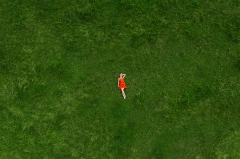 Slim Blonde Woman In Red Dress Lying On Green Grass Closing Her Face
