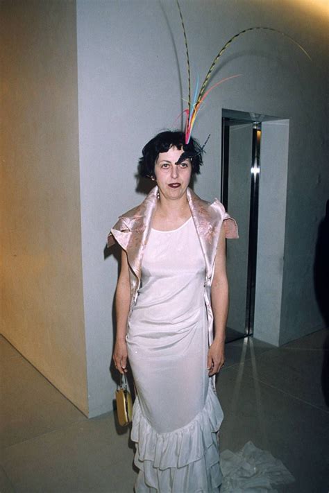A Woman In A White Dress And Feathered Headdress Poses For The Camera