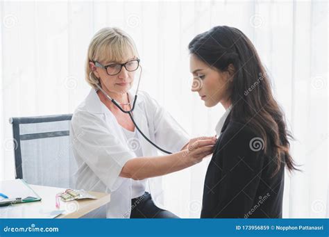 Senior Female Doctor Using Stethoscope Listening To Patients Heartbeat