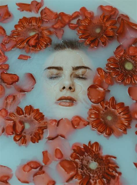 A Womans Face Is Surrounded By Flowers In A Water Bath With Red Petals