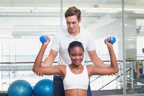 personal trainer helping client lift dumbbells on exercise ball stock image image of female