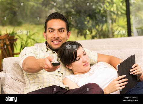 Cute Couple Cuddling In The Sofa While Watching Tv And Using Tablet