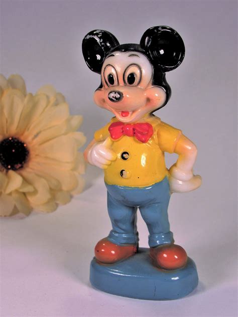 A Mickey Mouse Figurine Standing Next To A Flower