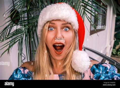 Funny Shocked Blonde Woman Wearing Santa Hat Looking Into Camera With Surprised Eyes And An Open