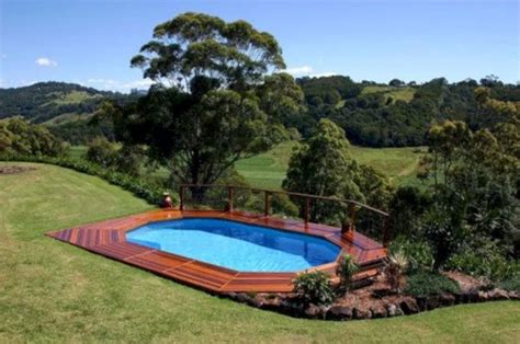 An Above Ground Swimming Pool Surrounded By Lush Green Hills And Trees With A Wooden Deck