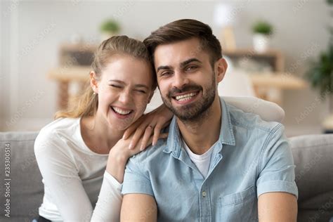 Portrait Of Smiling Young Husband And Wife Hugging Sitting On Couch