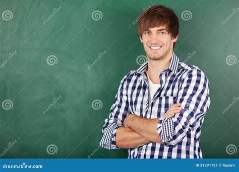 Male Teacher With Arms Crossed Standing Against Chalkboard Stock Image