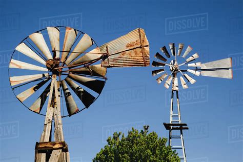 Close Up View Of Two Old Windmills Standing In The Yard Of A Farm
