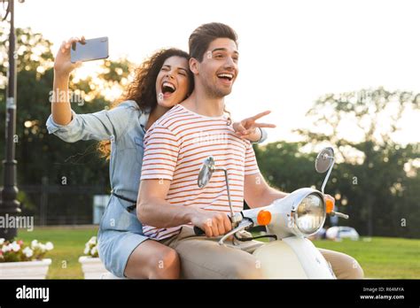 portrait of cheerful woman taking selfie on smartphone while riding on motorbike through city