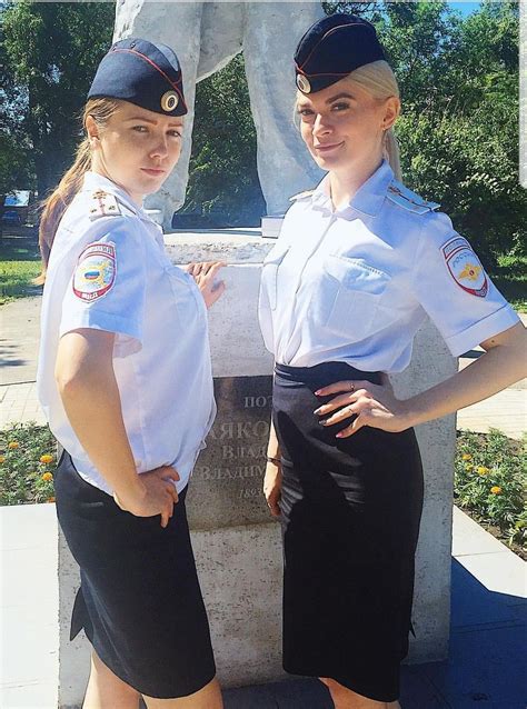 two women in uniform standing next to a statue with their hands on their hipss