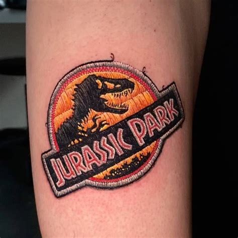 Jurassic Park Patch Tattoo Located On The Upper Arm