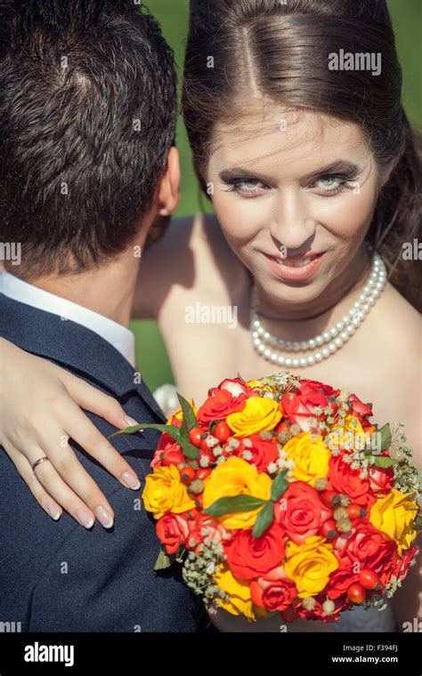 esposa abrazando a su esposo con el ramo en las manos en el pasto verde de fondo sonriendo