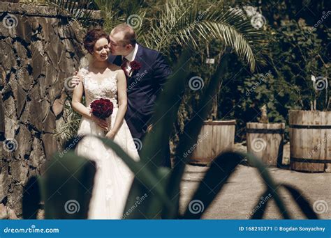 Cute Happy Groom Kissing Bride With Bouquet While Hugging Her From