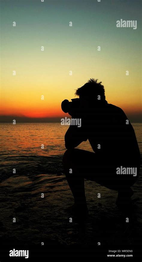 Silhouette Man Photographing Sea Against Sunset Sky Stock Photo Alamy