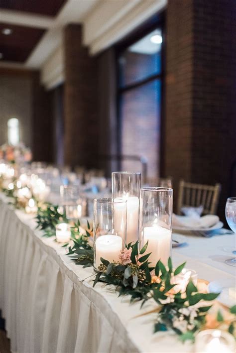 A Long Table With Candles And Greenery On It Is Set Up For A Formal