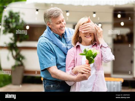 holiday celebration cheerful mature man surprising his wife with bouquet of flowers on