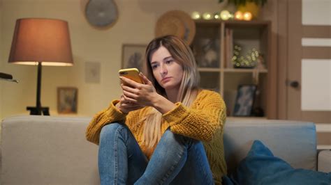 Tired Girl Sitting On The Sofa With Cell Phone Texting Message Bored