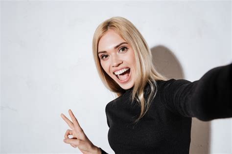 mulher excitada fazendo selfie e mostrando o gesto de paz no estúdio foto grátis