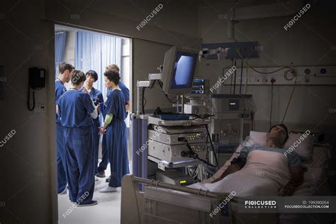 Patient Lying In Bed In Intensive Care Unit Team Of Doctors Discussing