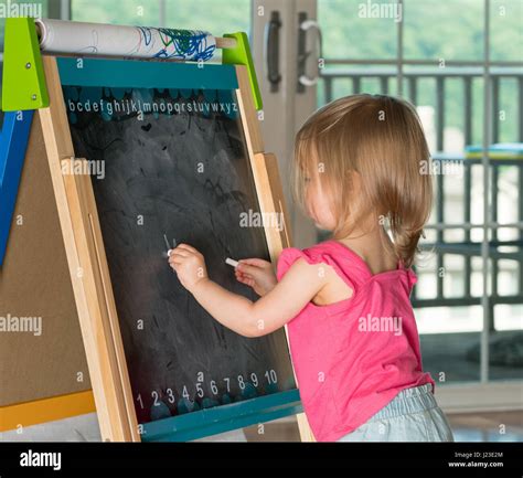 Young Child Learning To Write And Writing With Chalk On A Blackboard
