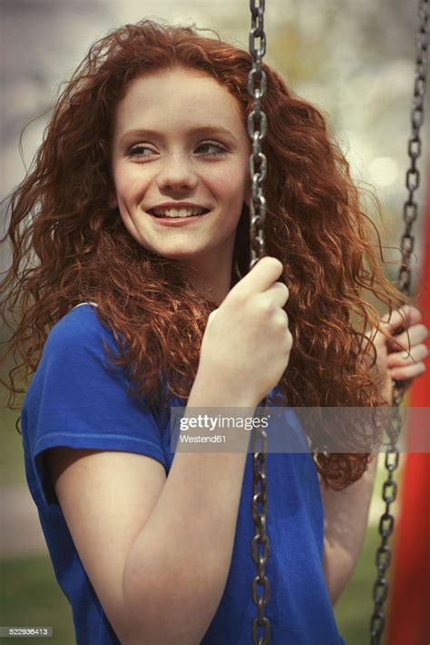 Portrait Of Smiling Girl With Curly Red Hair Sitting On A Swing High
