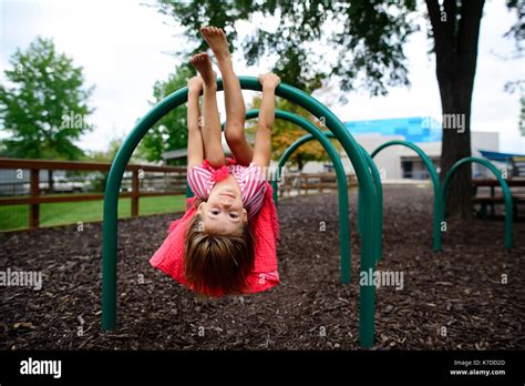 Portrait Of Girl Hanging Upside Down On Outdoor Play Equipment At