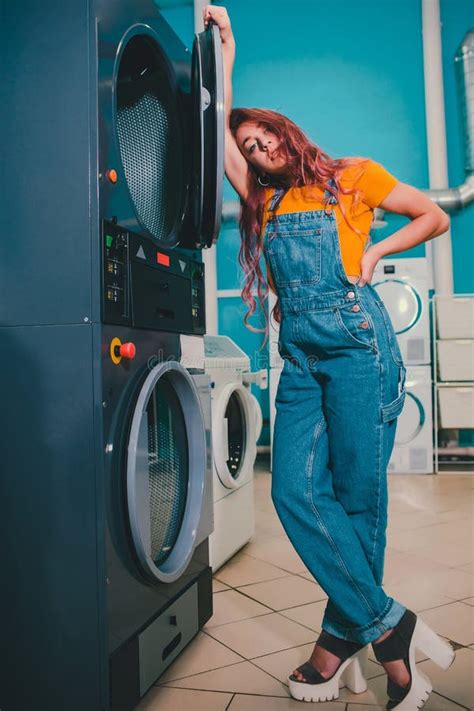 Young Woman Searching Clothes In Washing Machine Drum At Laundromat