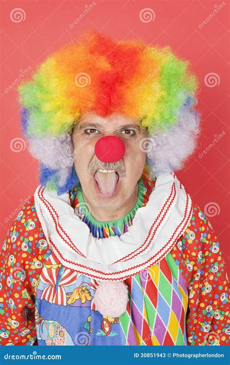 Portrait Of Senior Male Clown Sticking Out Tongue Over Red Background