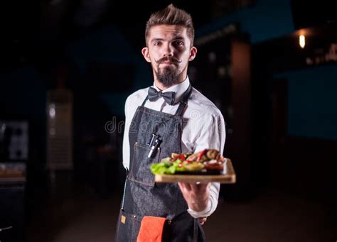 Young Waiter Helpfully Serves Dish In The Restaurant Stock Photo