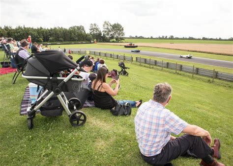 People Watching A Motorsport Race At A Race Track From A Grassed