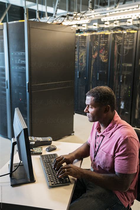 Black Male Technician Works At A Computer In A Server Room By Stocksy