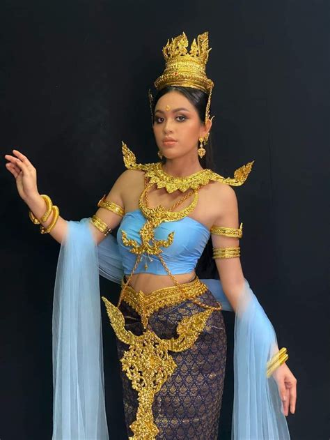 A Woman In A Blue And Gold Costume Standing Next To A Black Wall With