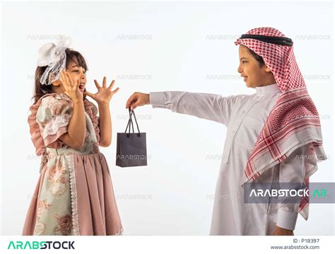 خلفية بيضاء لصبي وفتاه صغيران سعوديان مبتسمان ، الفتاه الصغيرة تضع يدها على خدها تشعر بالخجل