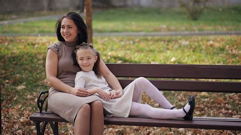 Young Mother And Daughter Are Resting In A City Park On A Bench A