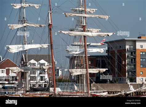 A Plane Landing At City Airport In East London Flies Over A Tall Ship
