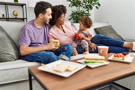 Couple And Daughter Having Breakfast Sitting On Sofa At Home Stock