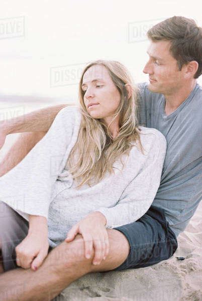 A Couple Sitting Close On A Beach A Man And Woman With Their Arms Around Each Other And Heads